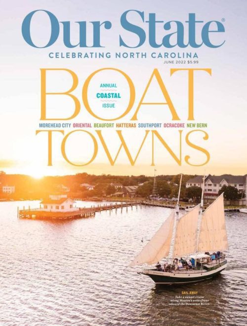 Magazine cover showing a sailboat on water with a coastal town in the background at sunset.